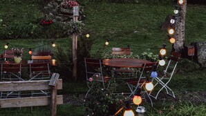 An outdoor seating area with wooden benches and a table, surrounded by greenery and string lights. - Gasthaus Hirsch (Wangen im Allgäu)
