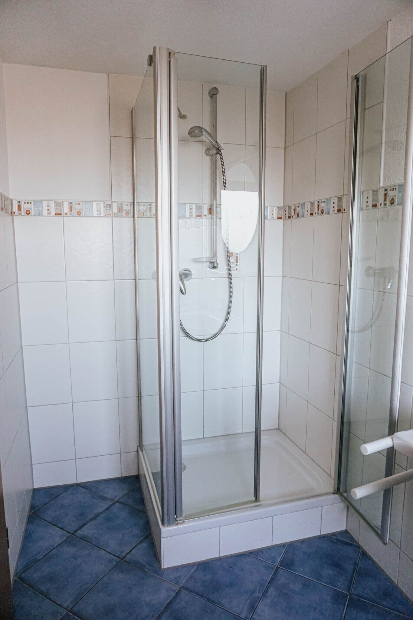 A glass-enclosed shower stall with a handheld showerhead and a wall-mounted control panel.