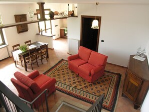 A spacious living area with a red sofa, a dining table with chairs, and a kitchen in the background. - Ca der Forn the Bread Oven House in Cascina Bricchetto Langhe - Italy (Trezzo Tinella)