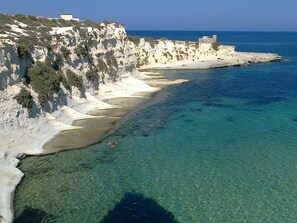 Un paysage côtier avec des falaises, une eau d’un bleu limpide et une plage.