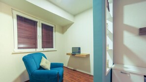 A small room with a blue armchair, a wooden floor, a white cabinet, and a shelf with a laptop.