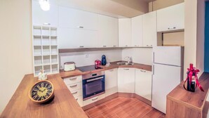 A compact kitchen with white cabinets, a wooden countertop, a built-in oven, and a refrigerator.