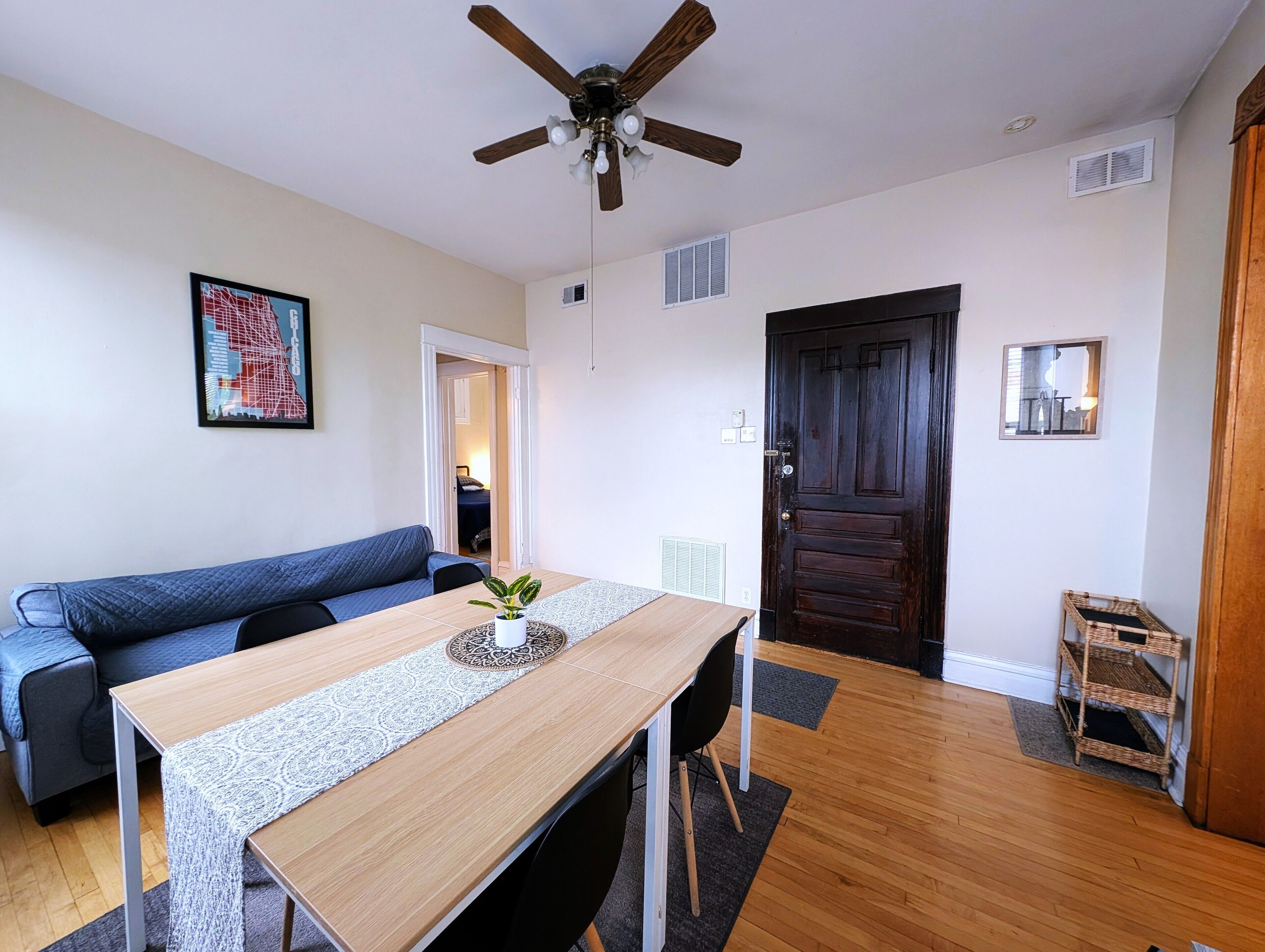 Un salon moderne avec une table à manger en bois, un canapé bleu, un ventilateur de plafond et une porte en bois foncé.