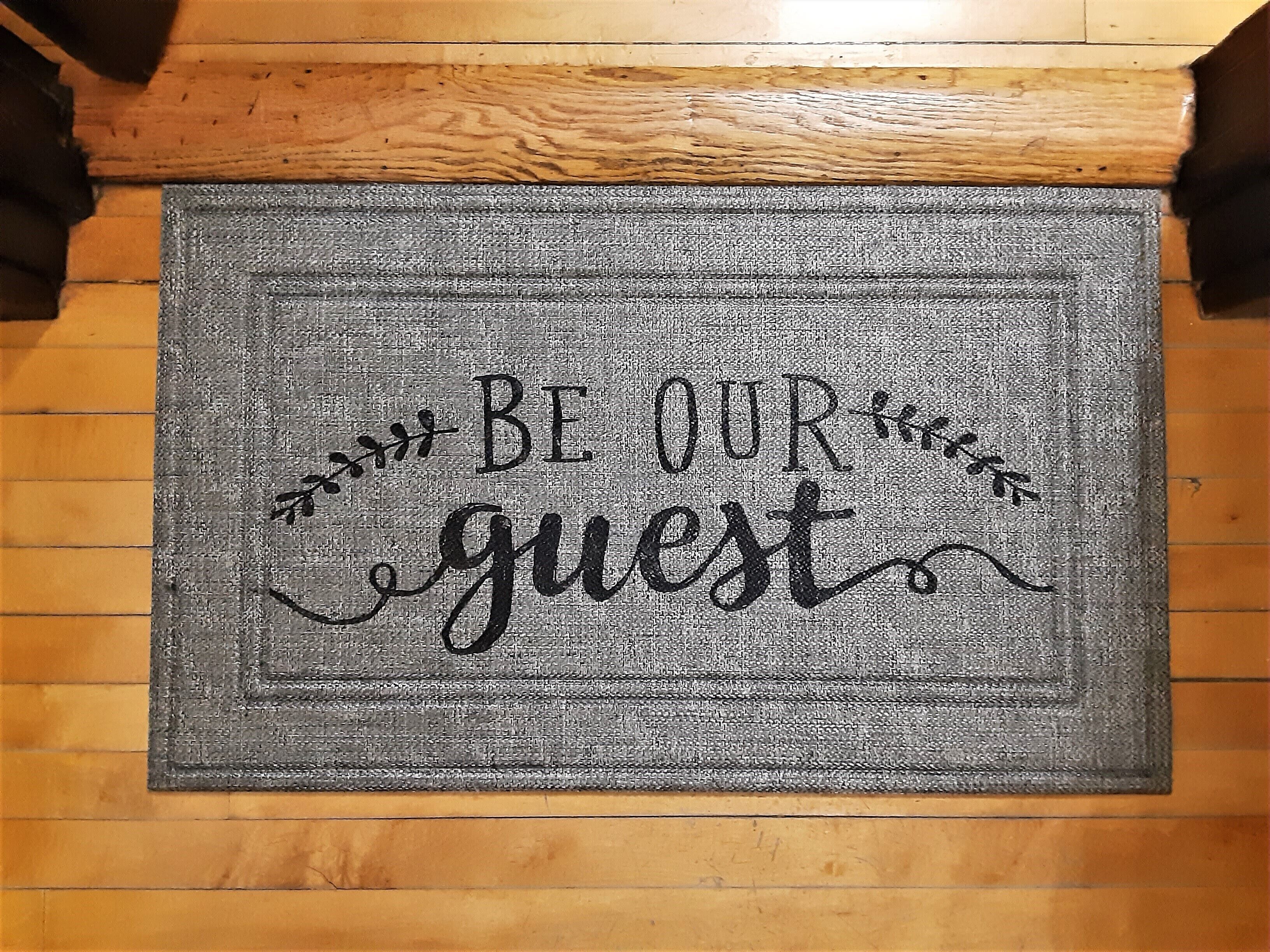 A doormat with the text "BE OUR guest" in a decorative font.