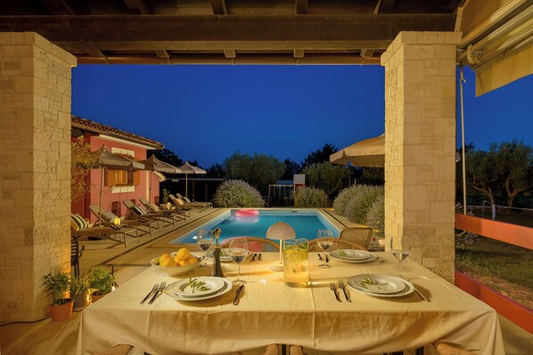 Un espace extérieur aménagé pour les repas, avec une piscine, des chaises longues et une table dressée pour un repas.