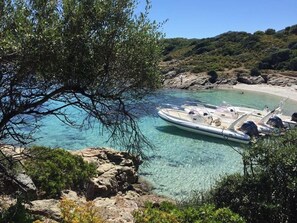 Un bateau était amarré près d’une côte rocheuse, dans une eau claire, entouré de verdure et avec une plage visible au loin.