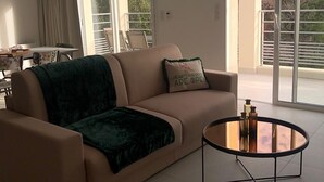 A modern living room with a beige sofa, a glass coffee table, and a view of a balcony with outdoor furniture. - RESIDENCE U MANELLU (Santa-Reparata-di-Balagna)