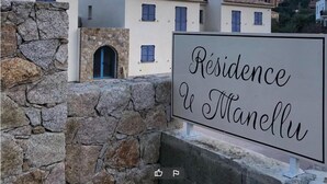 A sign for 'Residence a Manellu' with a stone wall and buildings in the background. - RESIDENCE U MANELLU (Santa-Reparata-di-Balagna)