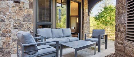 An outdoor patio with a stone wall, a grey sofa, two armchairs, and a coffee table.