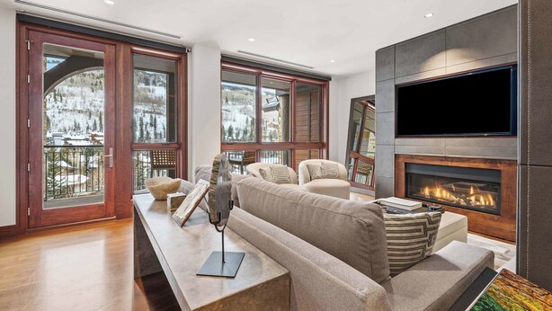 A modern living room with a fireplace, comfortable seating, and large windows offering a view of a snowy landscape.
