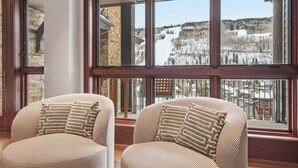 A room with two patterned armchairs facing a large window overlooking a snowy landscape.
