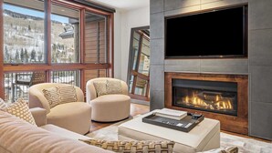 A modern living room with a fireplace, large windows, and a flat-screen TV.