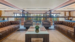 A spacious living area with leather sofas, a central coffee table, and a view of a stone building through large windows.