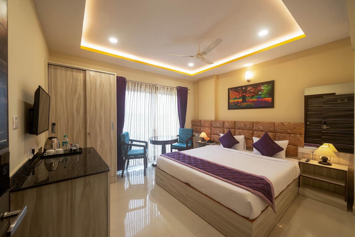 Quarto de hotel com cama, escrivaninha com cadeira, televisão, quadro e ventilador de teto.