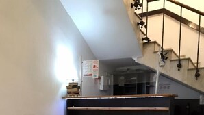 A reception area with a black reception desk, a bookshelf with books, a tiled floor, and a staircase in the background. - green classic (Tbilisi)