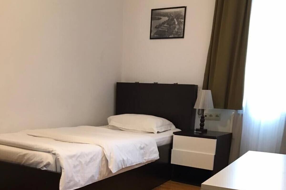 A simple, clean room with a bed, bedside table, and a small desk.
