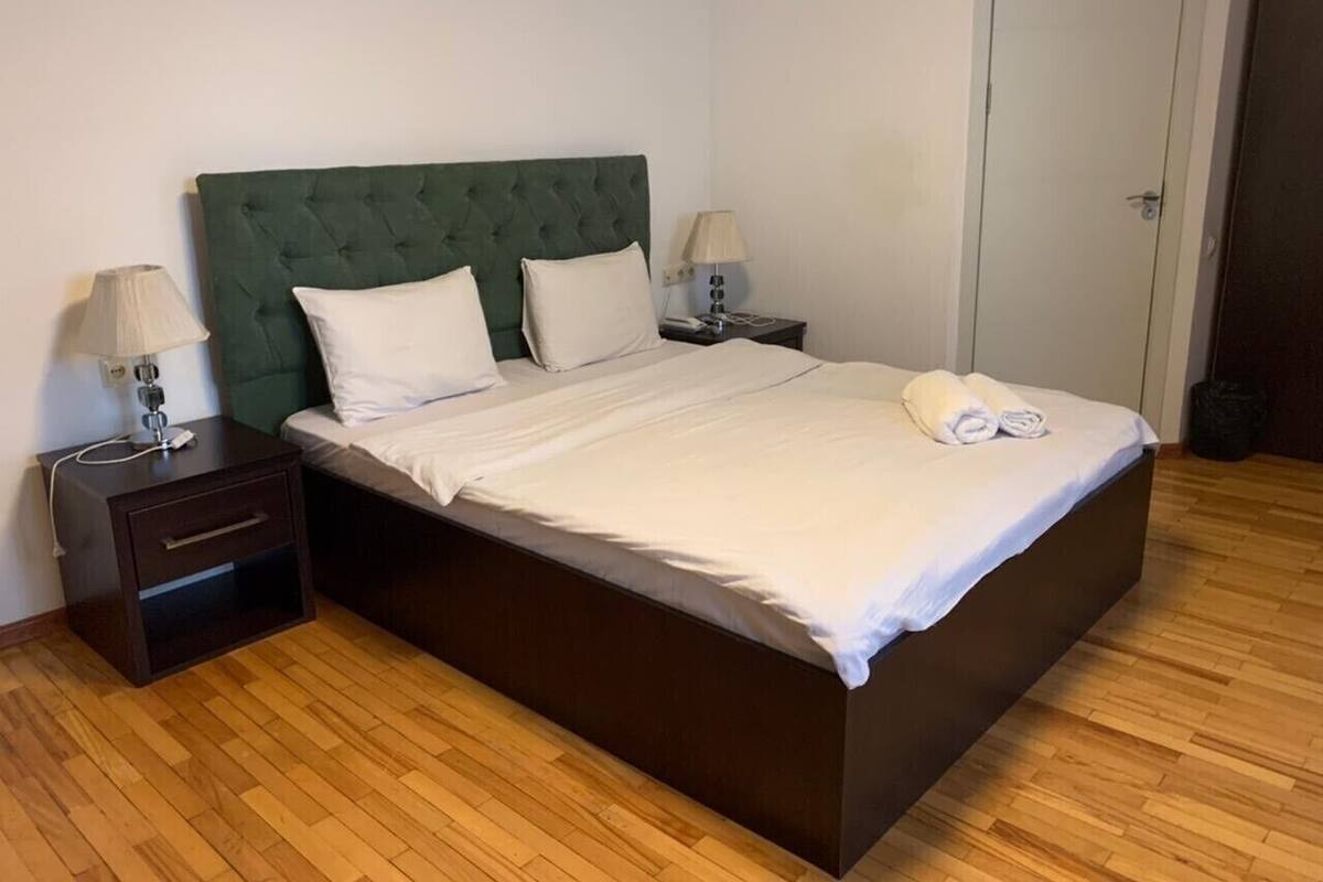 A single bed with a green upholstered headboard, two bedside tables with lamps, and a wooden floor.