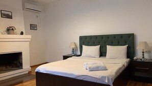 A neatly arranged bedroom with a large bed, a fireplace, and two bedside tables with lamps. - green classic (Tbilisi)