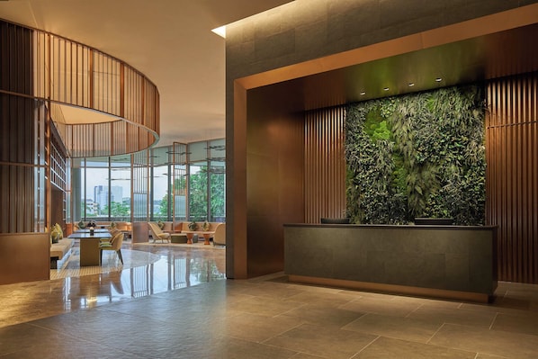 A modern lobby with a curved staircase, a reception desk with a green wall, and seating areas.