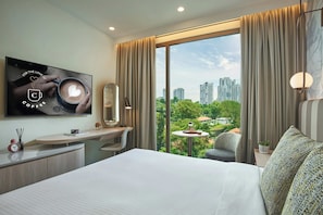 A modern hotel room with a large bed, a desk, a chair, a TV, and a view of a cityscape.