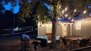 Een terras buiten met een eettafel en stoelen, een barbecue en lichtslingers.