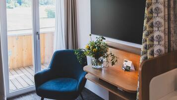 A modern room with a large window, a blue chair, a wooden desk, a television, and a small potted plant.