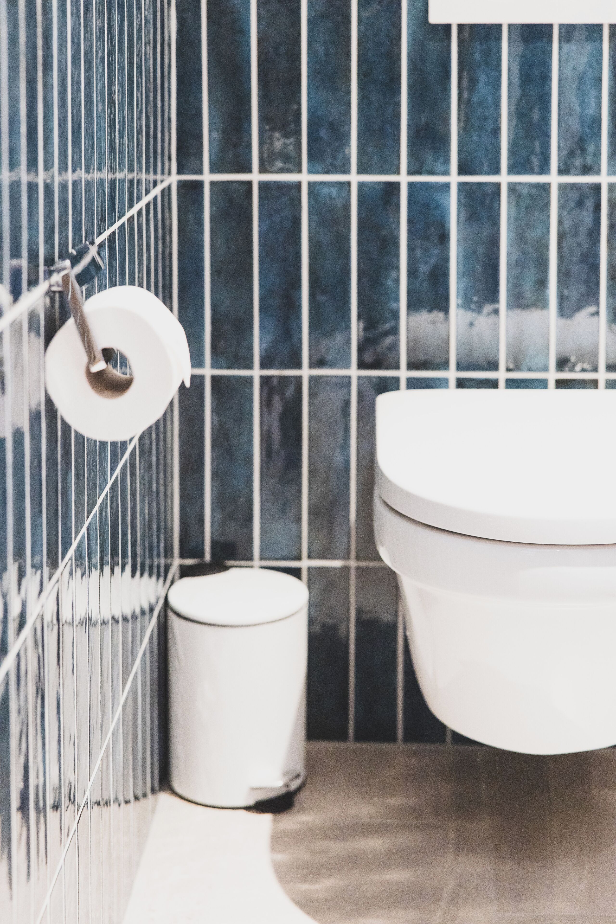 Un baño con inodoro, un dispensador de papel higiénico y un bote de basura.
