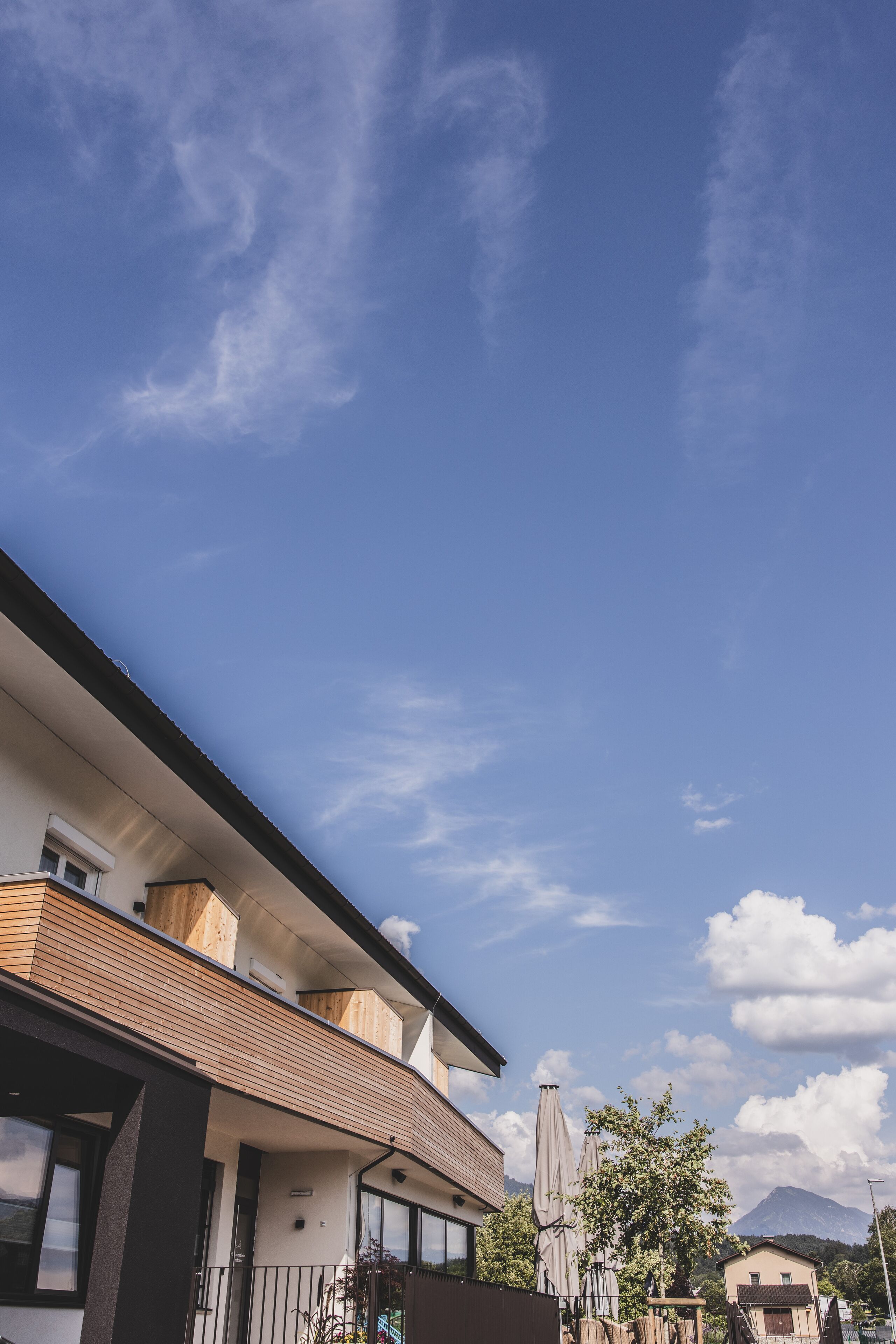 Un bâtiment moderne à deux étages, doté d’un balcon et d’une façade en bois, avec une montagne en arrière-plan.