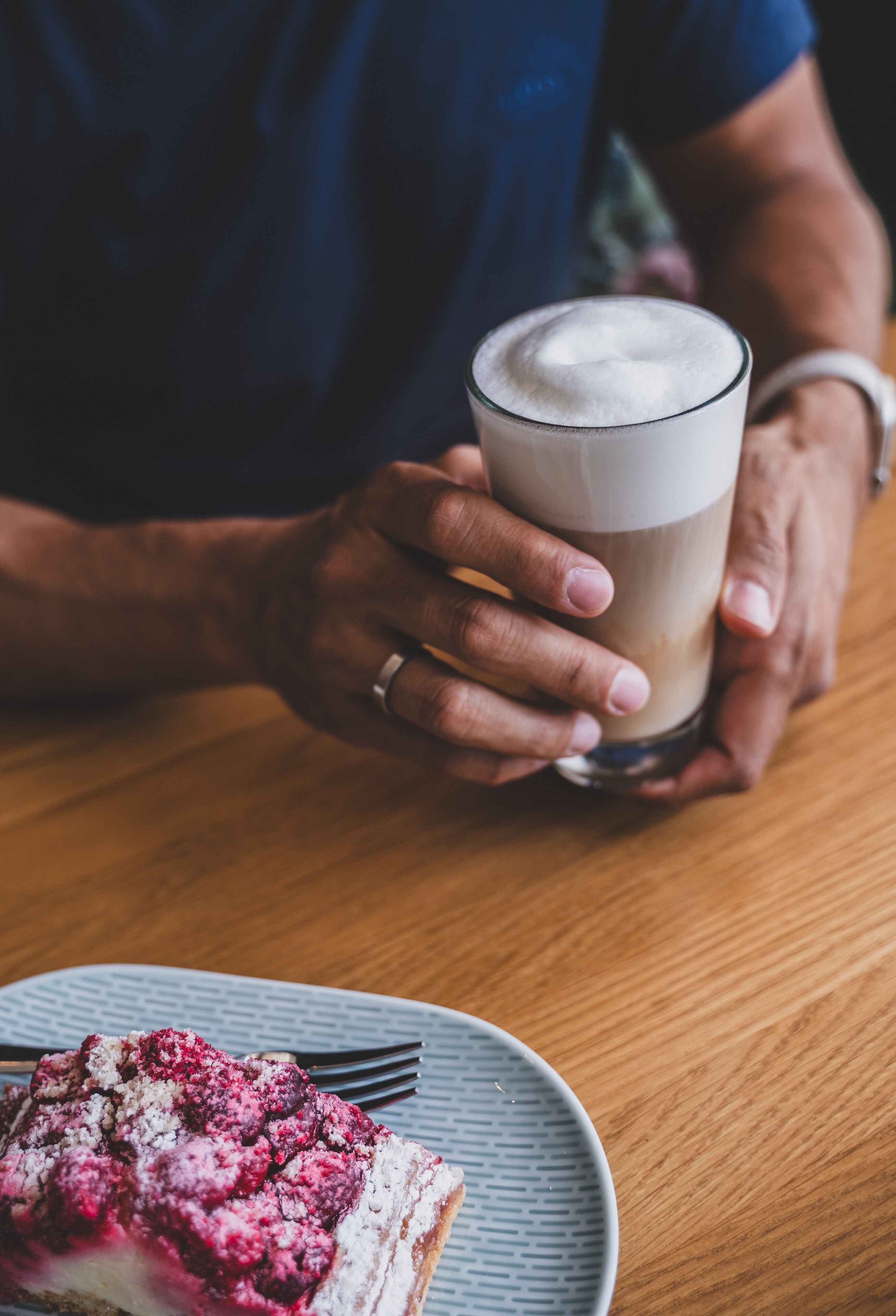 Une personne tenant une tasse de café, une assiette avec un dessert et une fourchette sur une table en bois.