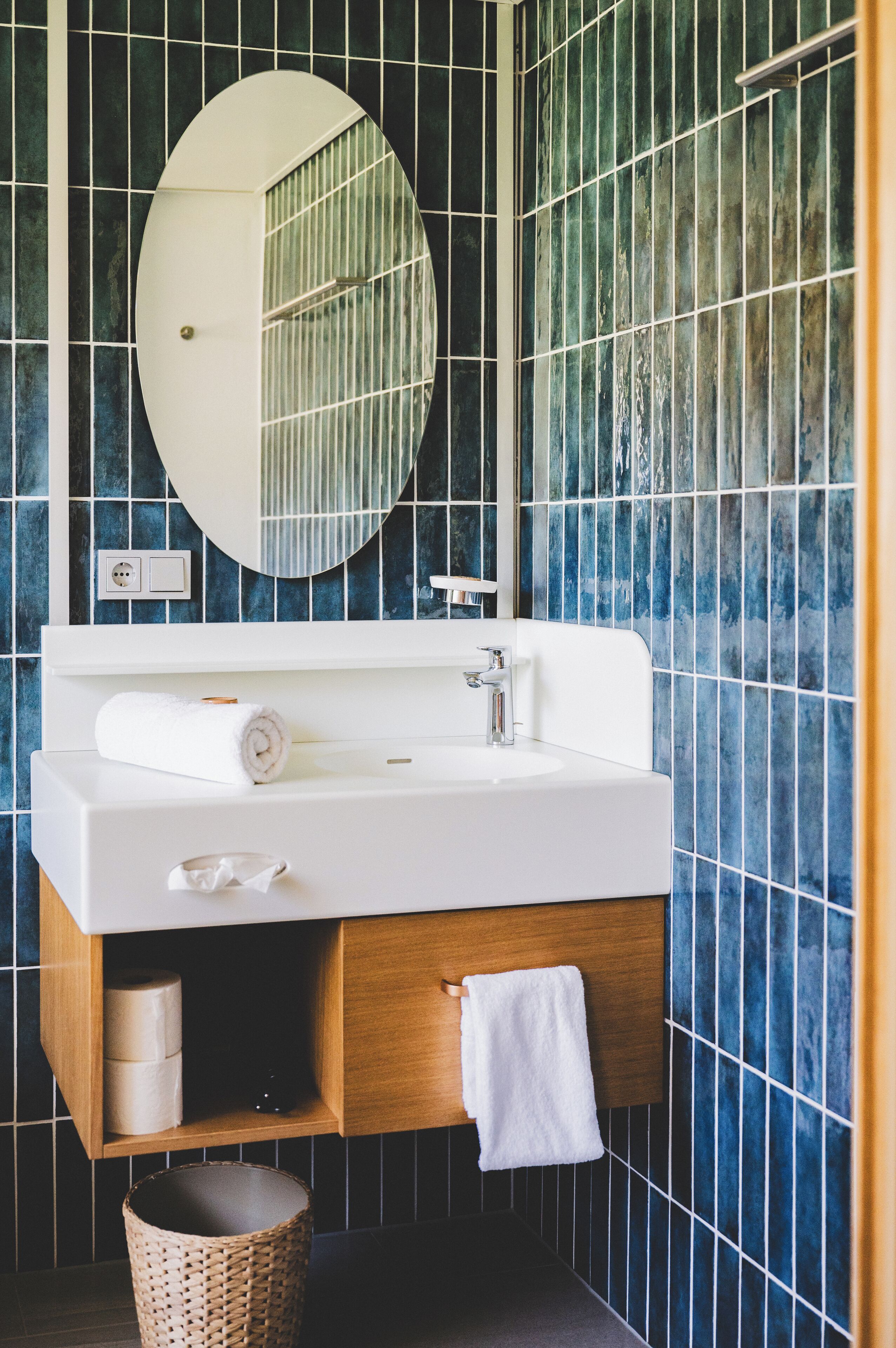 Ein Badezimmer mit einem weißen Waschbecken, einem runden Spiegel und einem Holz-Waschtisch.