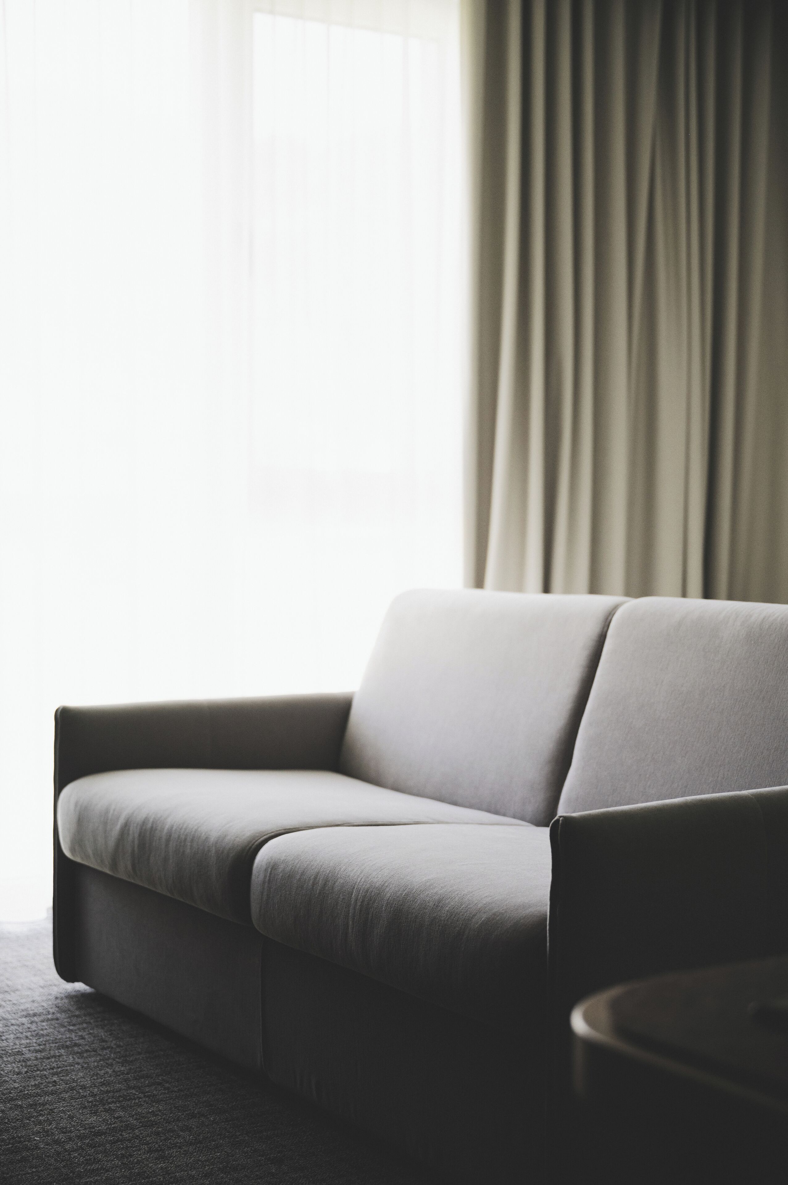Una sala de estar moderna con un sofá gris, una mesita redonda y un ventanal con cortinas.