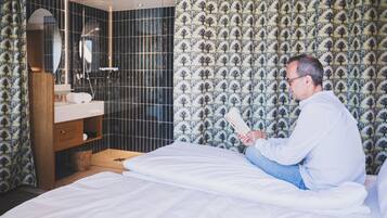 Ein Hotelzimmer mit Bett, einem Nachttisch aus Holz, einem Spiegel, einem Badezimmer mit Dusche und Wandpapier mit Muster.