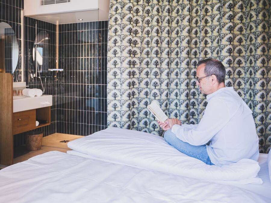 Ein Hotelzimmer mit Bett, einem Nachttisch aus Holz, einem Spiegel, einem Badezimmer mit Dusche und Wandpapier mit Muster.