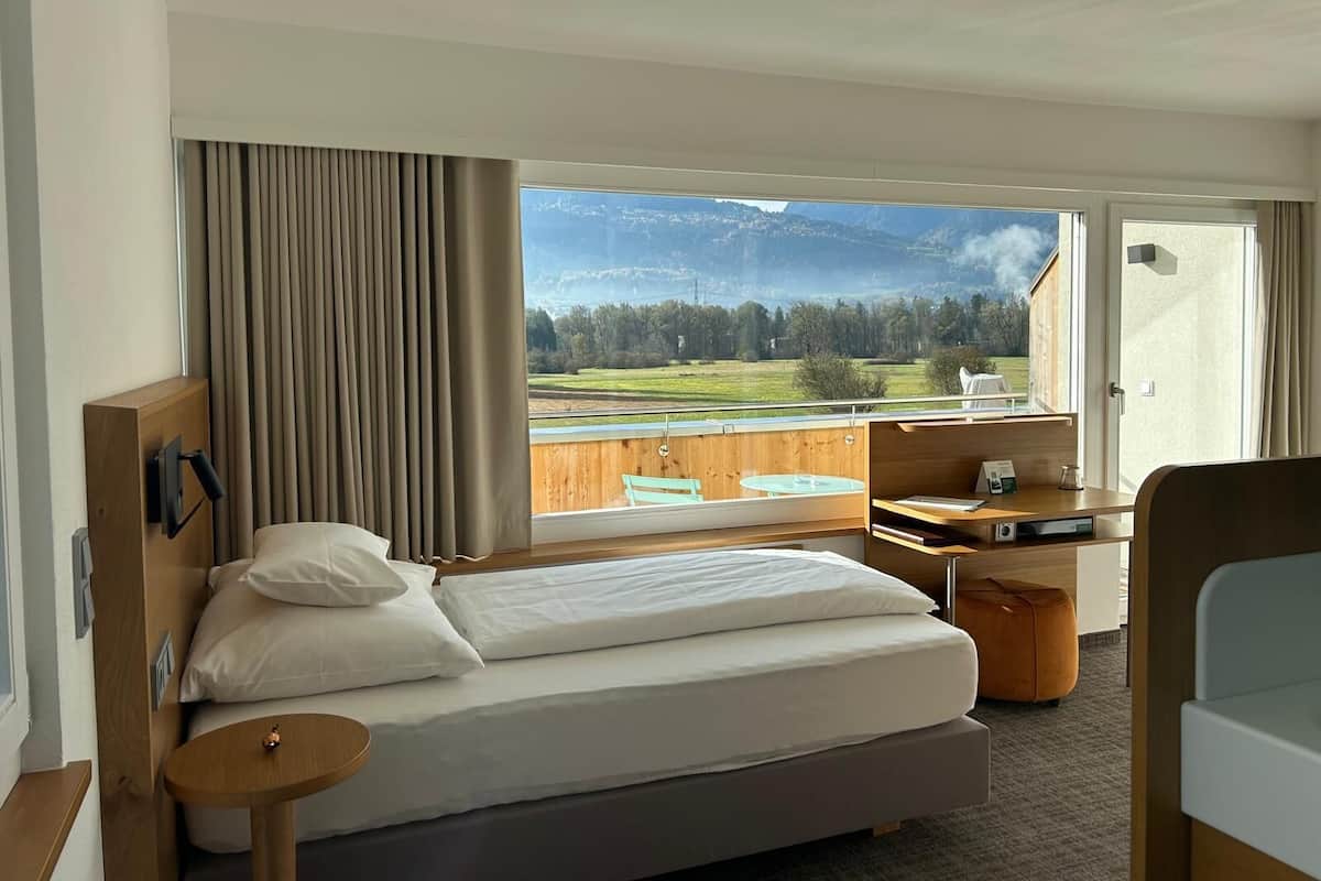 Una habitación de hotel moderna con una cama, un escritorio y vistas a un paisaje montañoso.