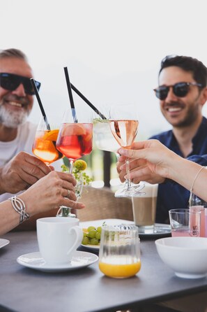 A table with a white cup, a glass of orange juice, a glass of pink drink, and a bowl of grapes. - TILL Naturhotel Self-Check-In (Satteins)