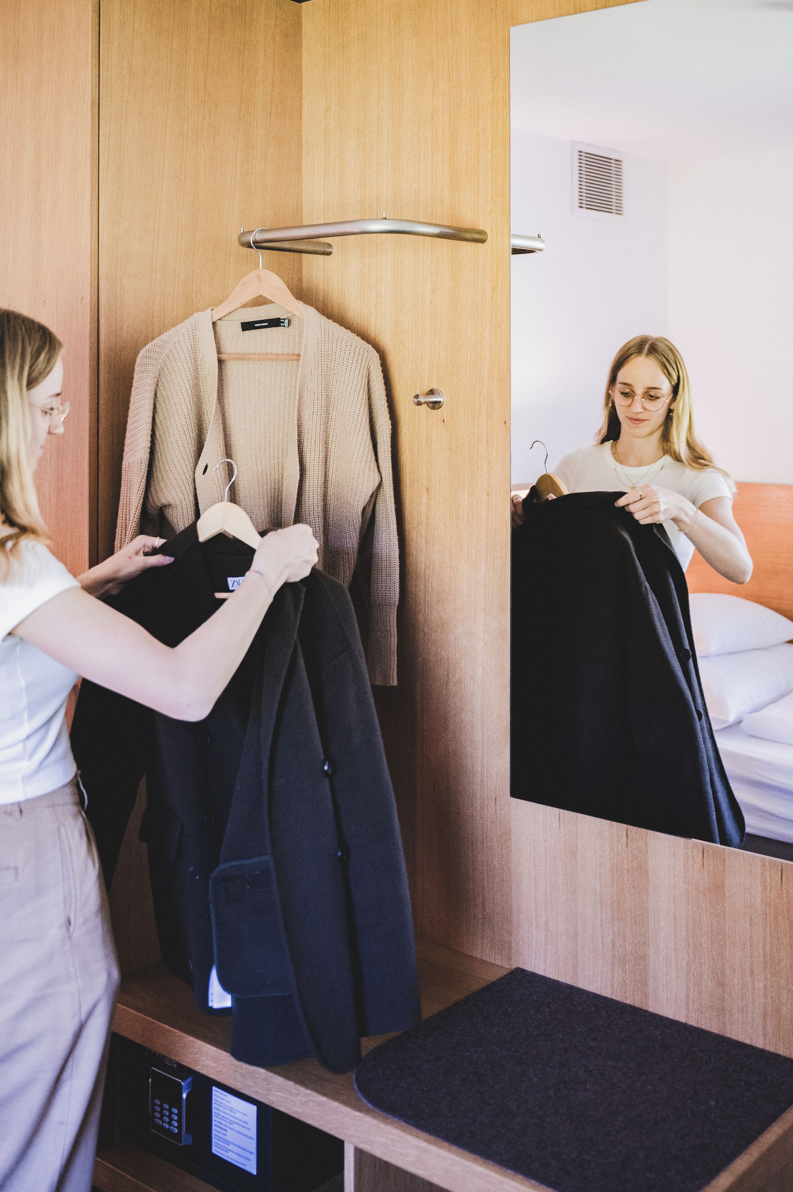 Ein Hotelzimmer mit Holzschrank, Bett mit weißer Bettwäsche und Spiegel, der einen Teil des Raumes widerspiegelt.