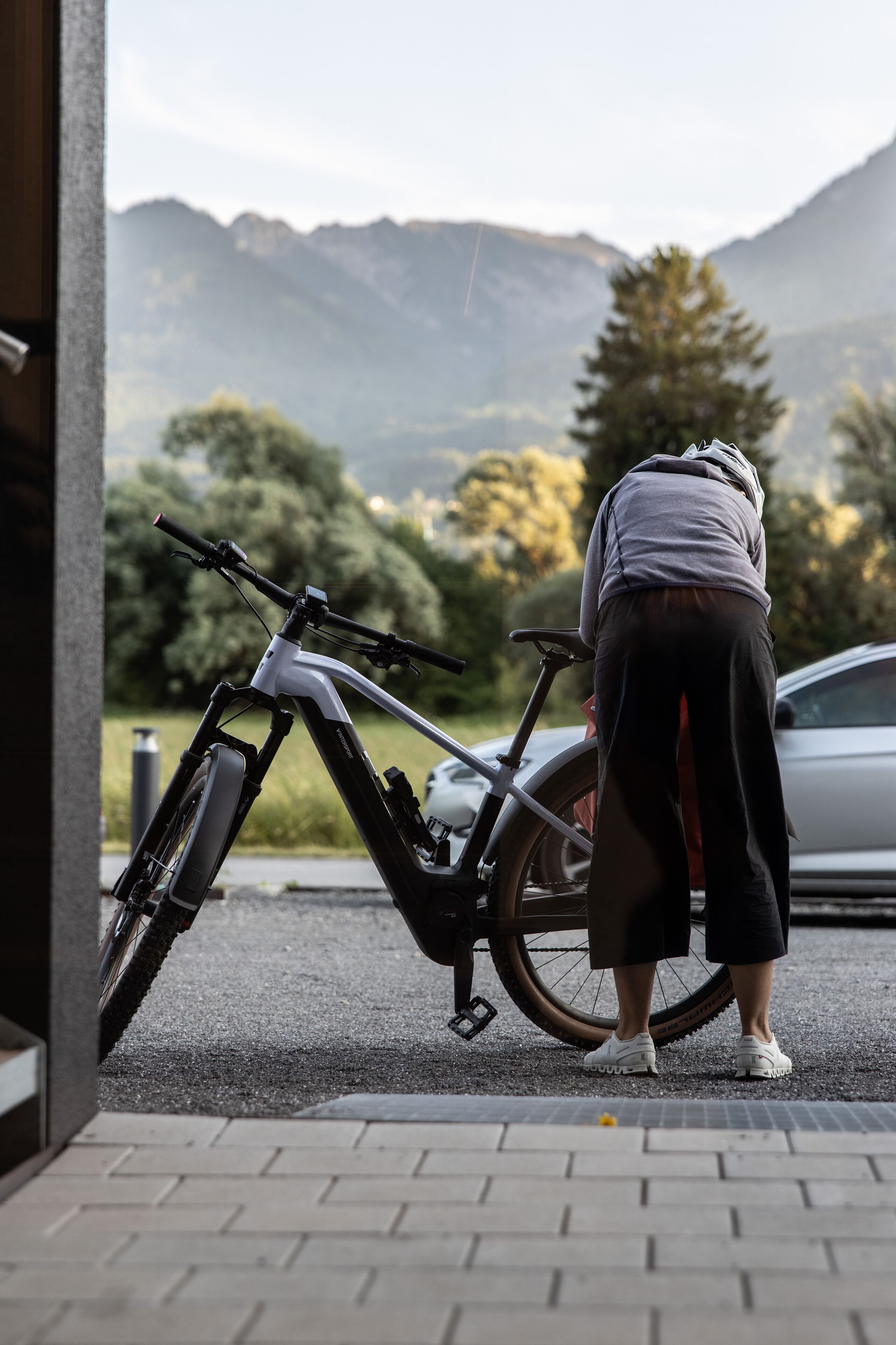 A person leaning on a bicycle in an outdoor setting with a mountain view in the background.