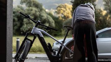 A person leaning on a bicycle in an outdoor setting with a mountain view in the background.