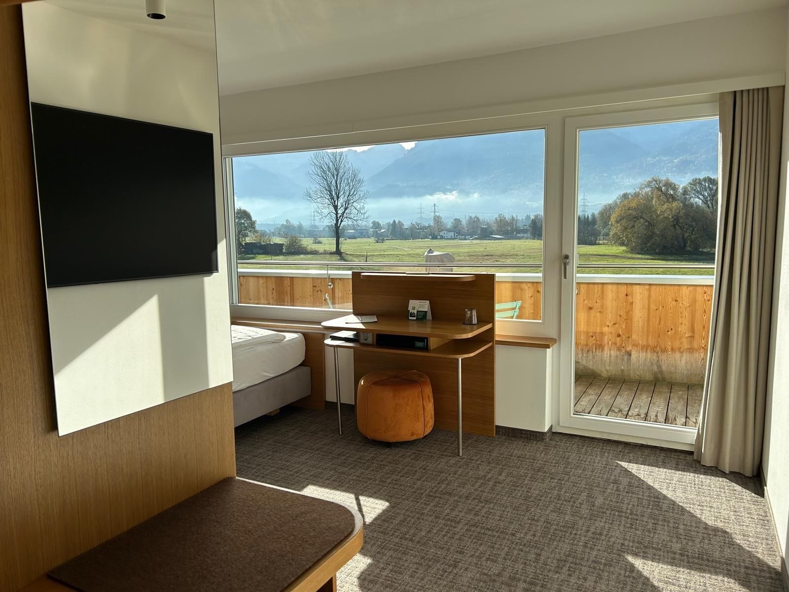 A modern room with a bed, a desk, and a large window offering a view of a green landscape.