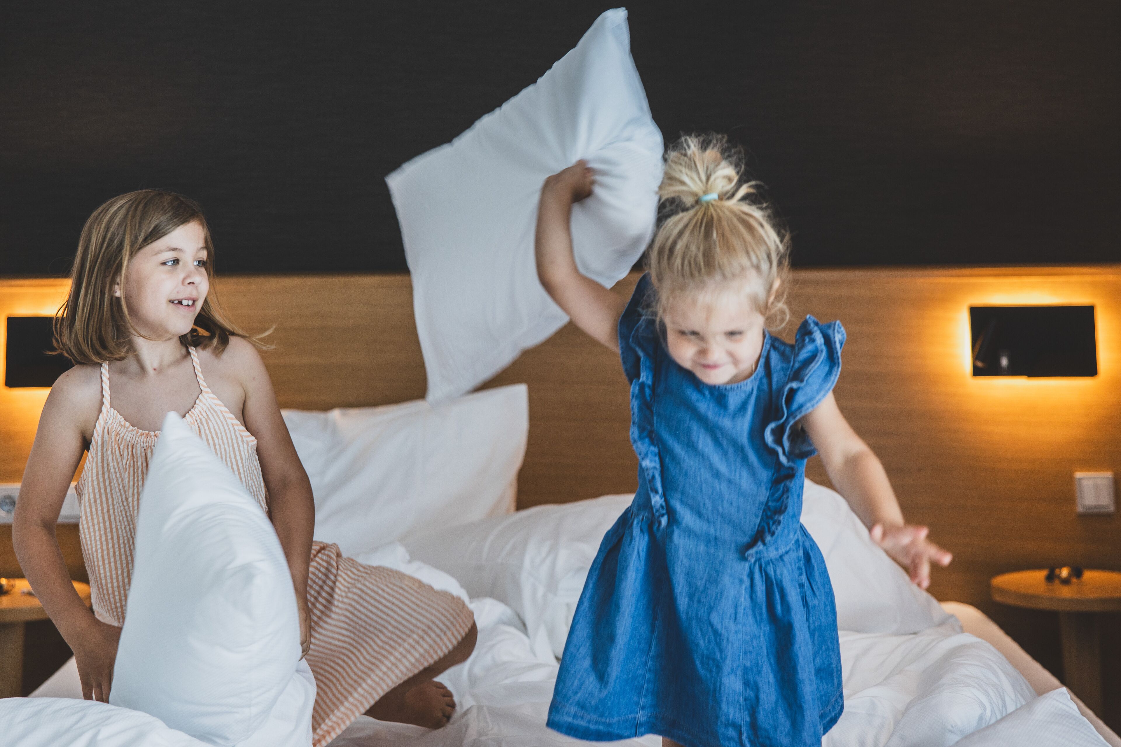 Two children playing with pillows on a bed in a hotel room.