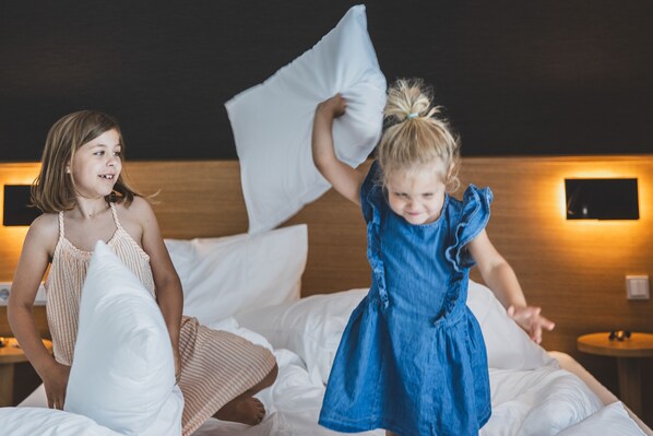 Two children playing with pillows on a bed in a hotel room.