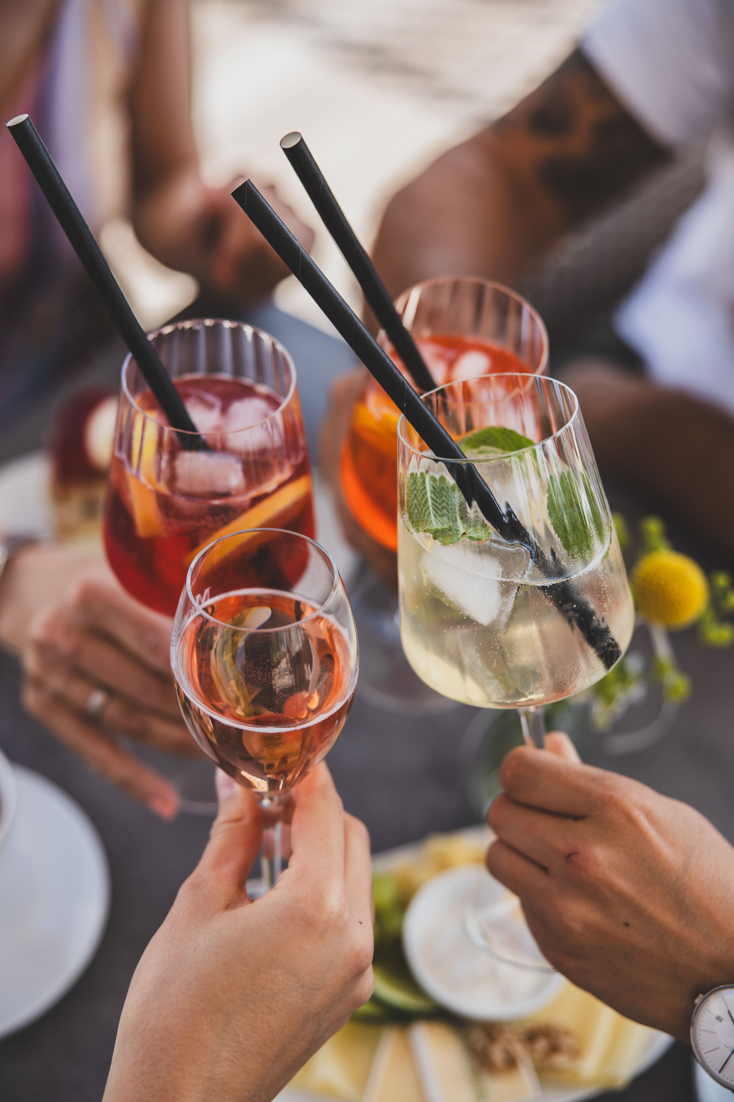 A group of people toasting with drinks, glasses with straws, and a glass with ice cubes and mint leaves.