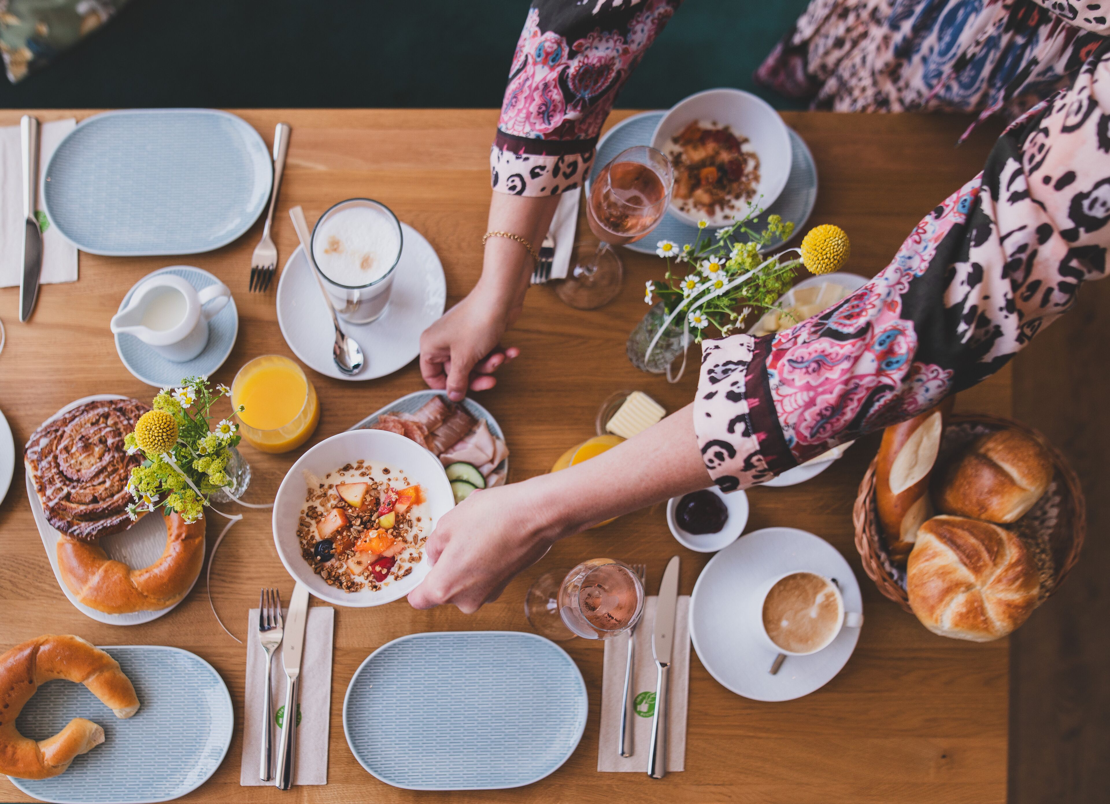 A breakfast setting with various dishes, including pastries, fruits, and beverages, arranged on a wooden table.
