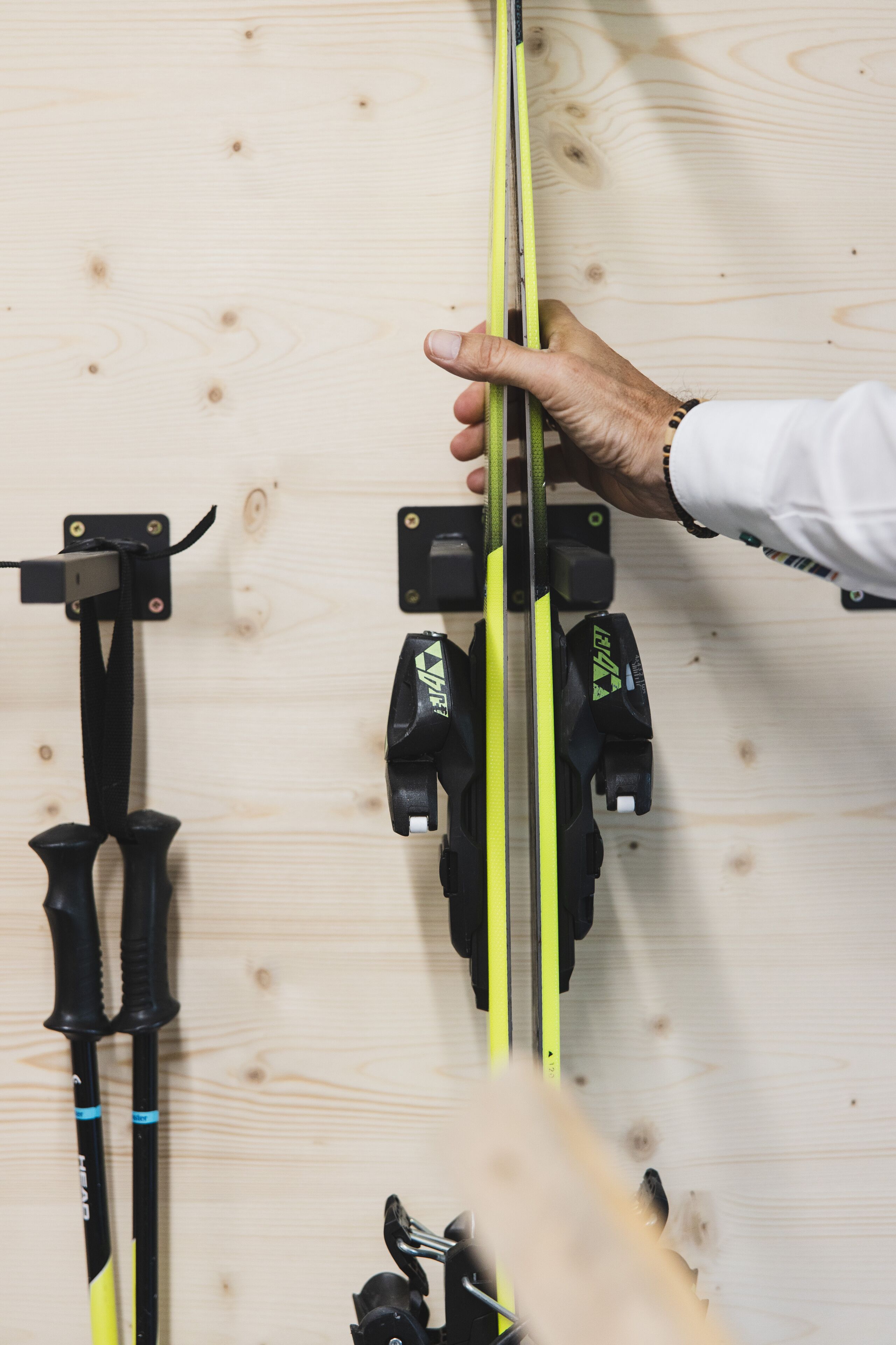 A hand holding a pair of skis against a wooden wall with ski racks.