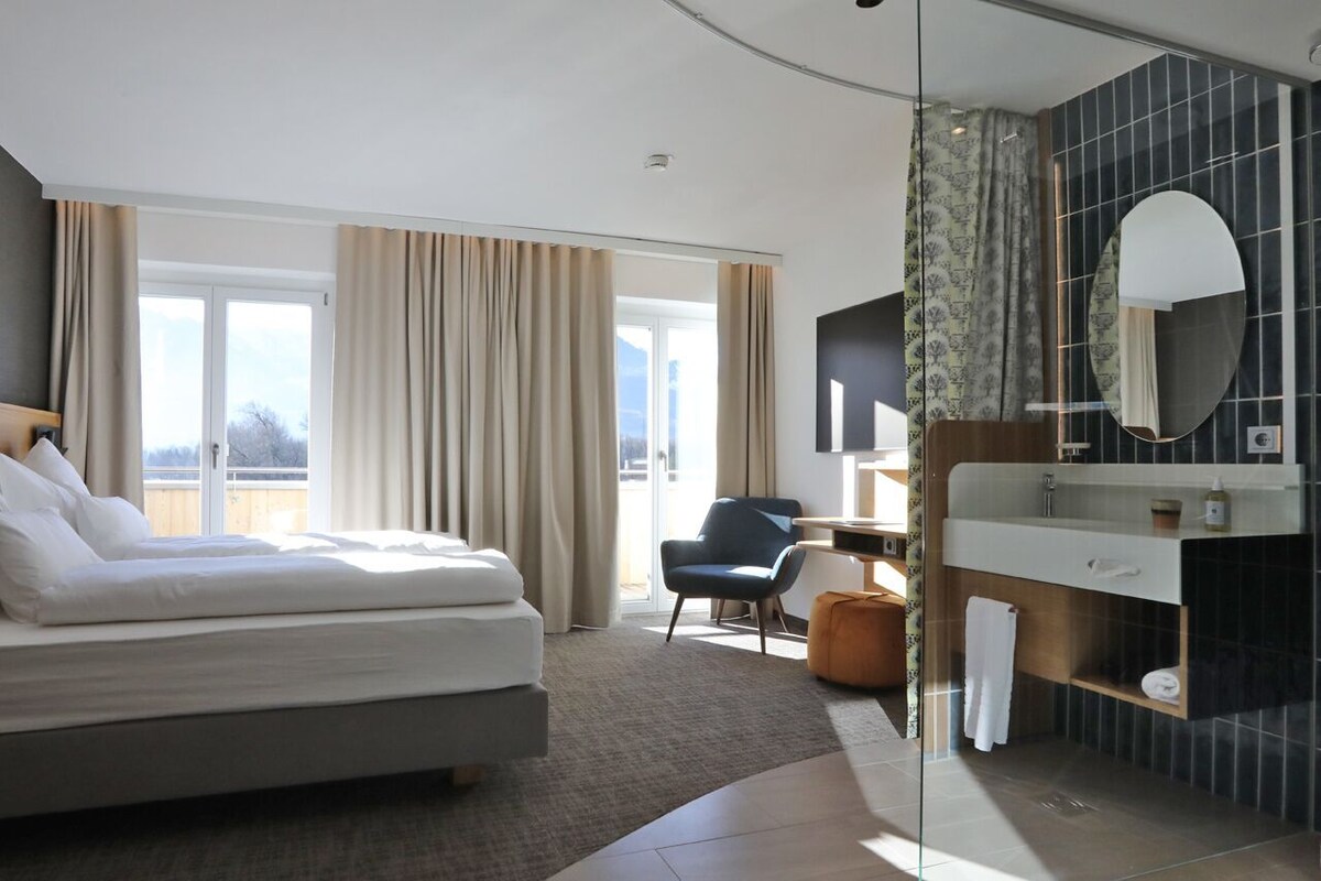 Une chambre d’hôtel moderne équipée d’un lit, d’un bureau, d’une chaise, d’une salle de bain avec un miroir et offrant une vue sur l’extérieur.