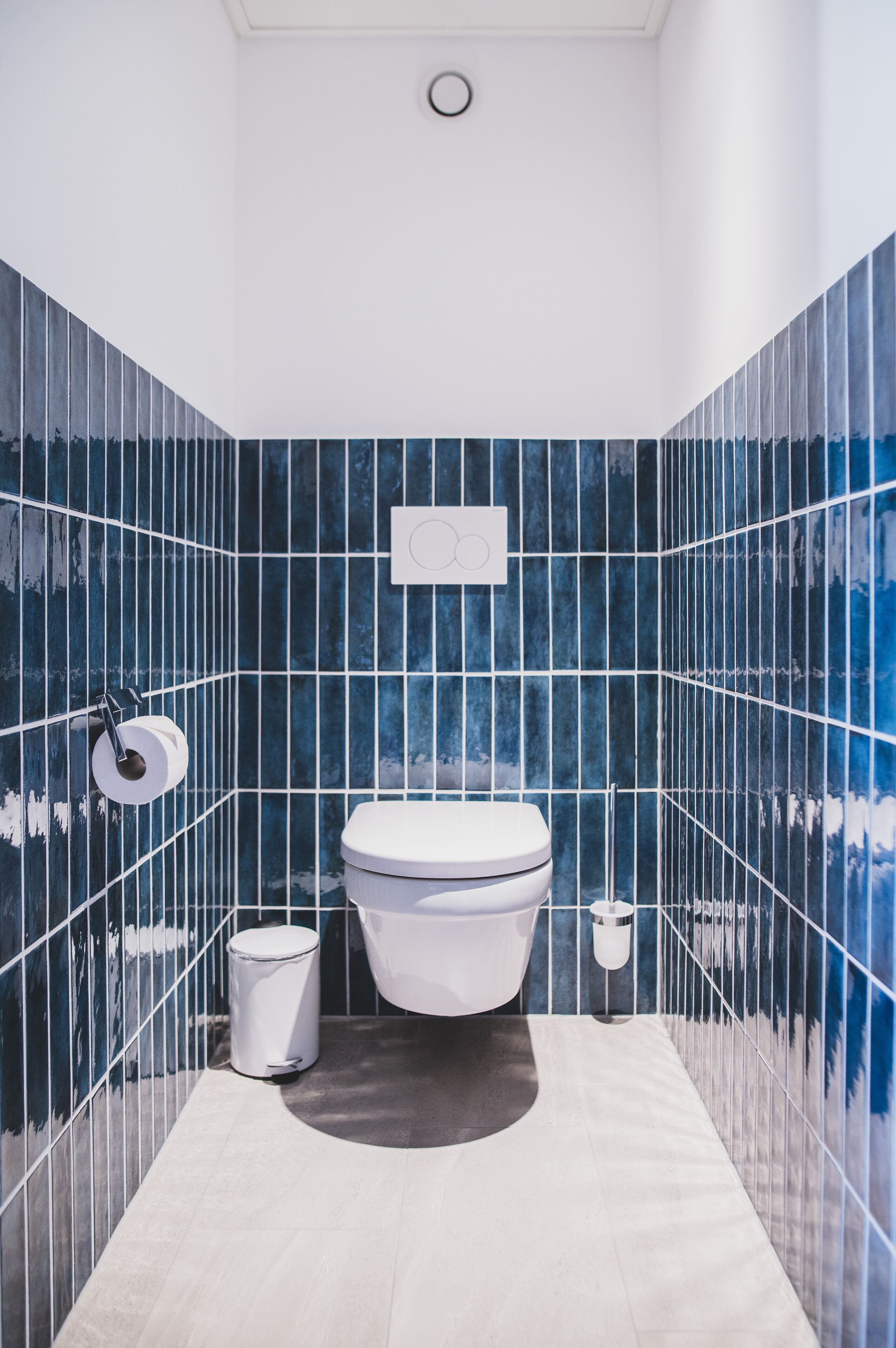 Un baño moderno con inodoro blanco, paredes con azulejos azules y piso blanco.