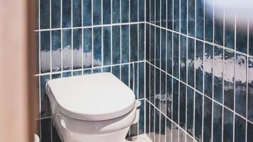 A bathroom with a white toilet, blue-tiled walls, and a white floor.