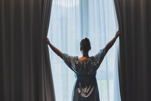 A person standing by a window with curtains, arms raised. - TILL Naturhotel Self-Check-In (Satteins)