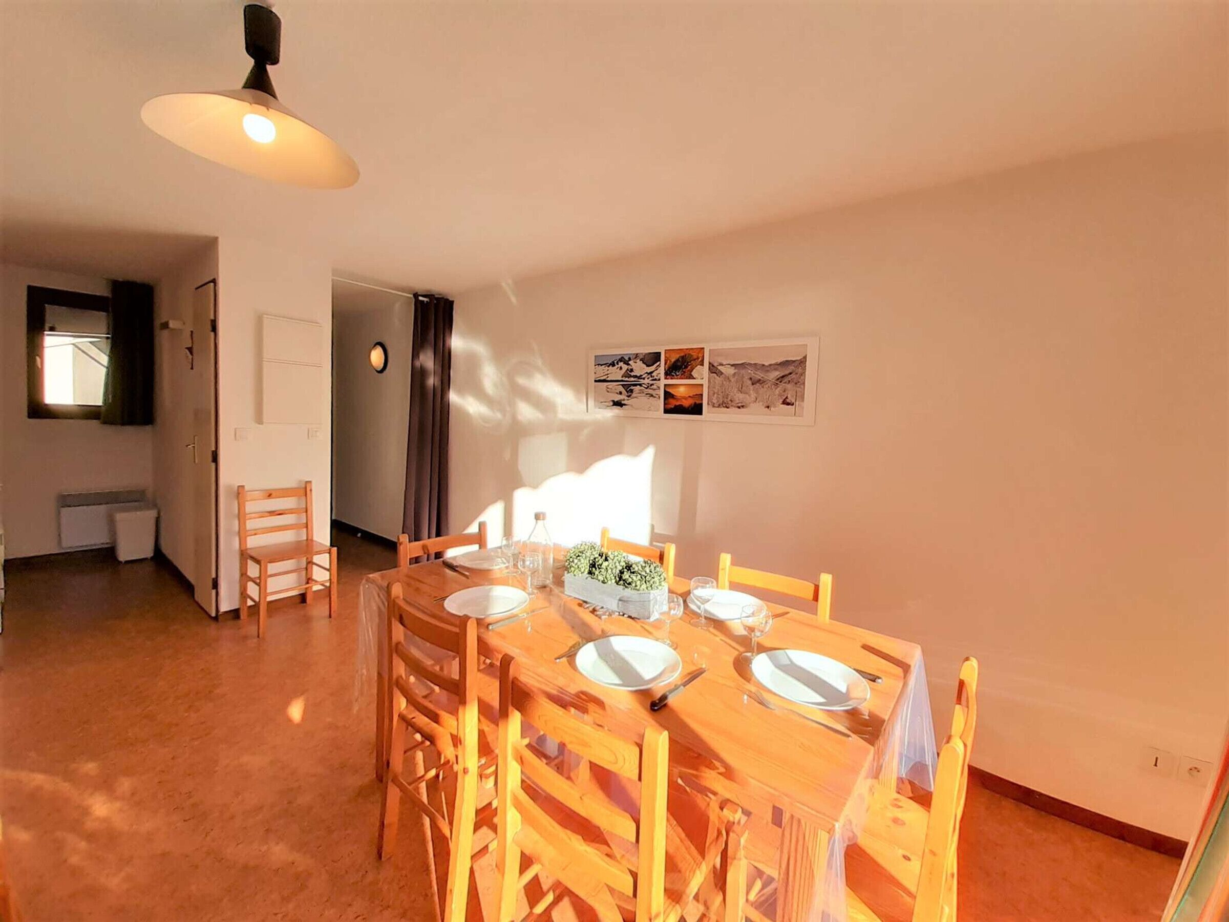 Un coin repas avec une table en bois, dressée pour quatre personnes, entourée de chaises. Un luminaire est suspendu au-dessus de la table.