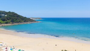 Une plage avec une eau d’un bleu limpide, un rivage sablonneux et une colline parsemée de bâtiments.
